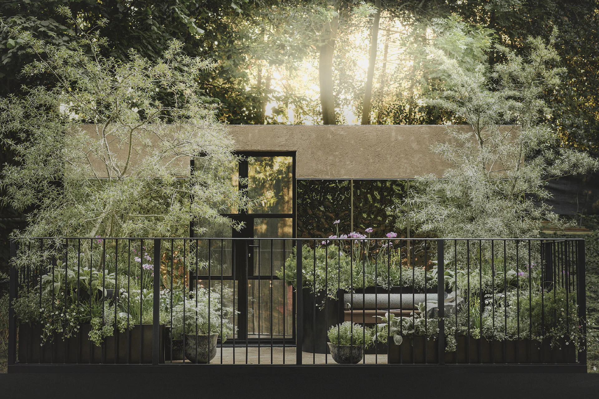 Visualisation of the balcony garden behind black railings, with trees and planters in evening light